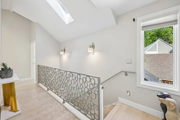 Architectural metal railing, skylight, wall-mounted sconces, wood-finish flooring, and white window trim