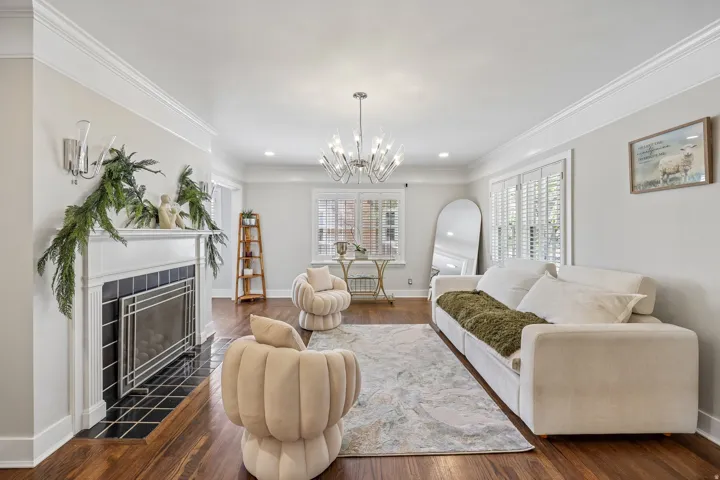 Fireplace with black tile surround, wood-finish flooring, white plantation shutters, and crown molding