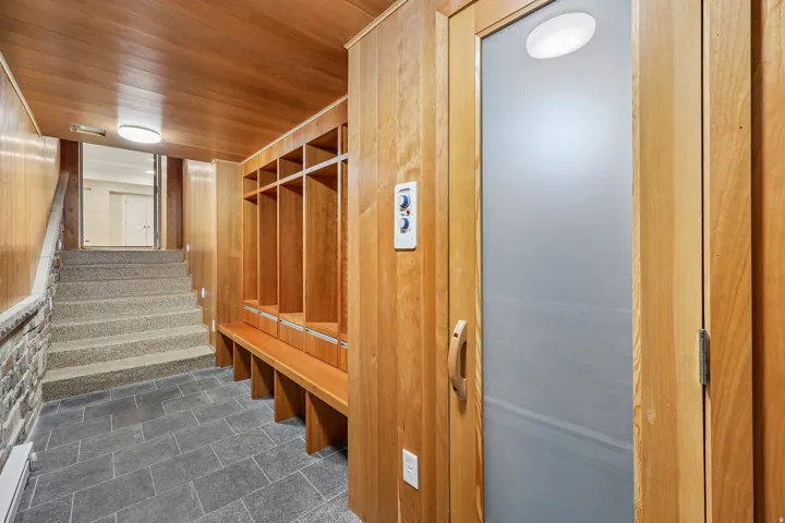 Wood-paneled walls and ceiling, built-in wooden bench with storage cubbies, stone-clad wall accent, tiled flooring, and an elevator with a frosted glass door