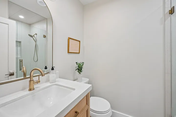 Floating vanity with a light wood-finish, featuring a white rectangular sink and brass-finish faucet