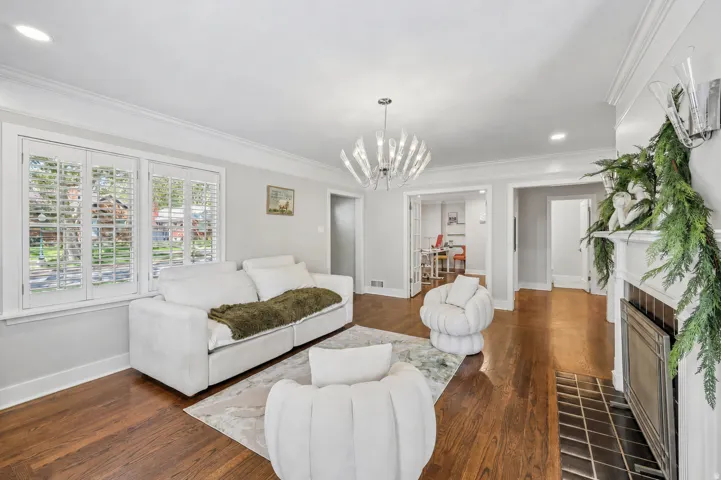 Hardwood flooring throughout, crown molding, double windows with plantation shutters, fireplace with tile hearth, and a modern chandelier