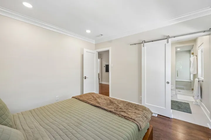 Recessed lighting, crown molding, wood-finish flooring, white barn door, and a walk-in shower with a built-in bench