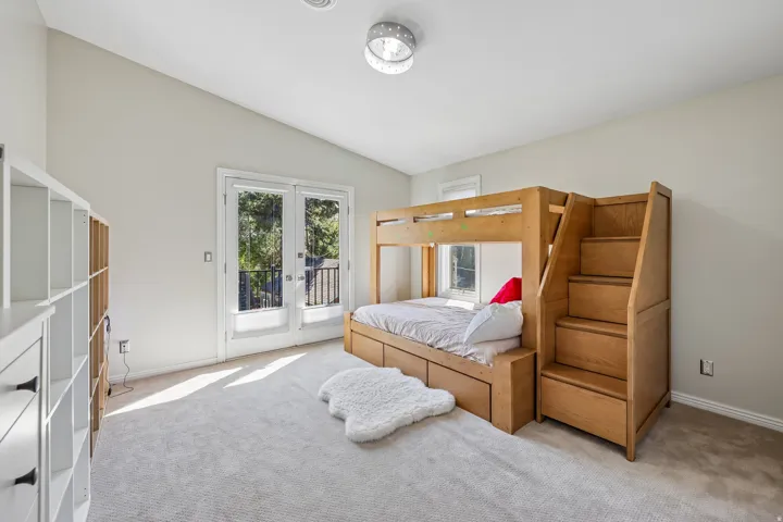 Vaulted ceiling with a flush-mount light fixture, carpet flooring, and double French doors opening to an exterior balcony with a black railing