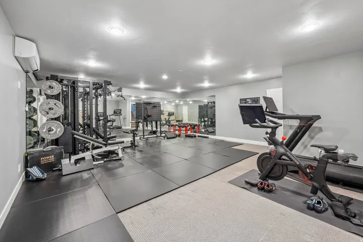 State-of-the-art home fitness center featuring professional-grade multi-station strength training equipment, stationary cycling bike with digital console, dark tile flooring throughout, recessed LED ceiling lighting, and ample open space for functional tr