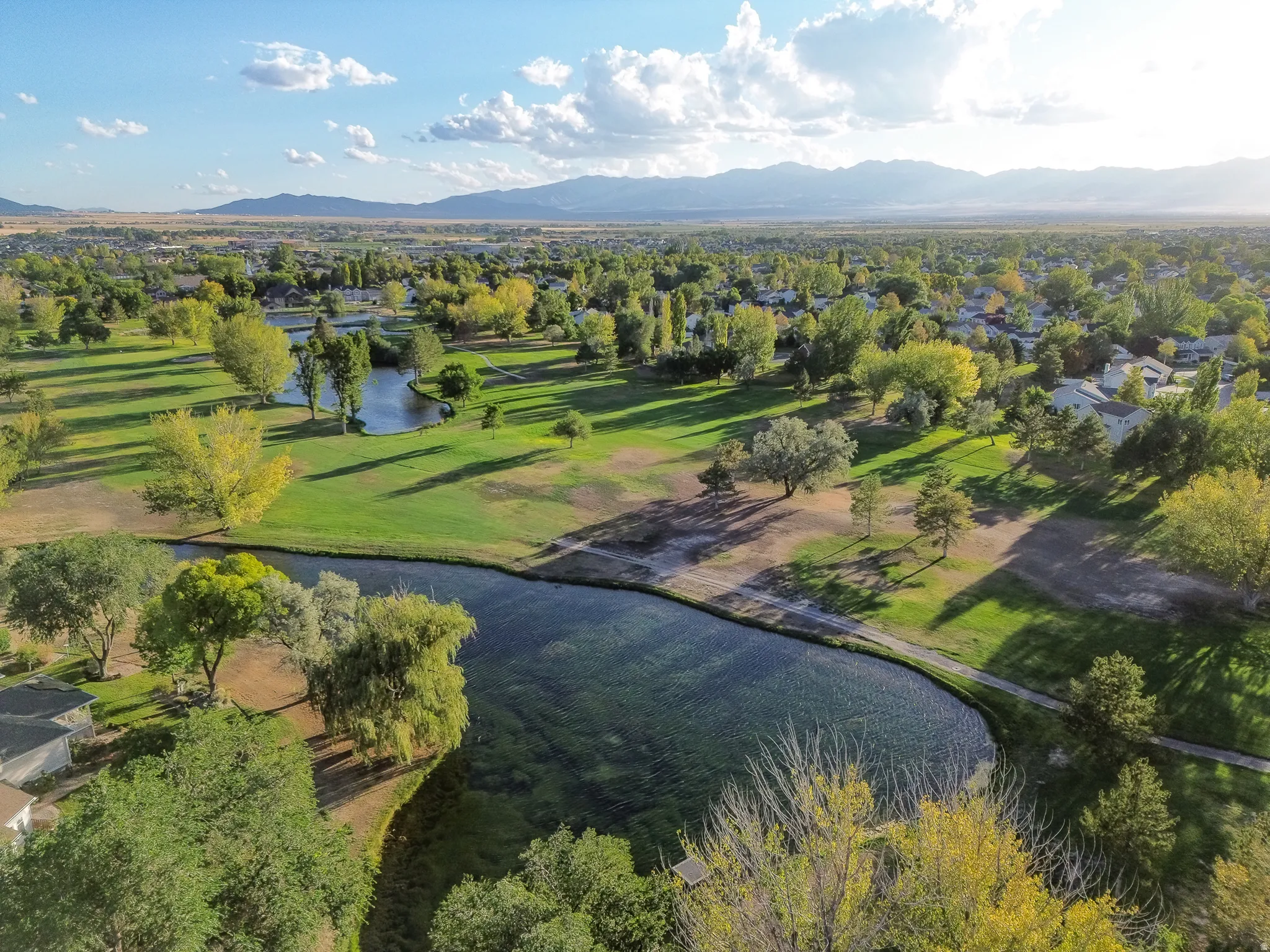 Expansive green spaces with mature trees, multiple water features, and distant mountain scenery