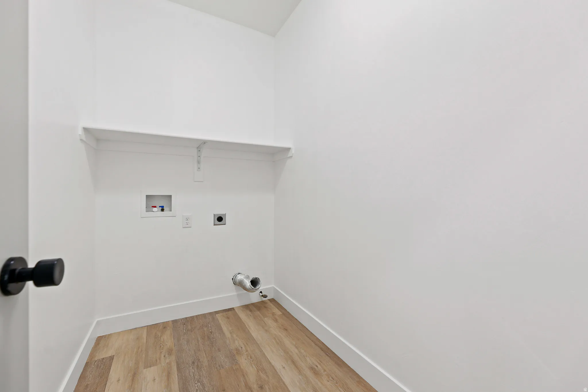 Laundry area featuring wood-finish flooring, white walls, built-in shelving, and utility hookups
