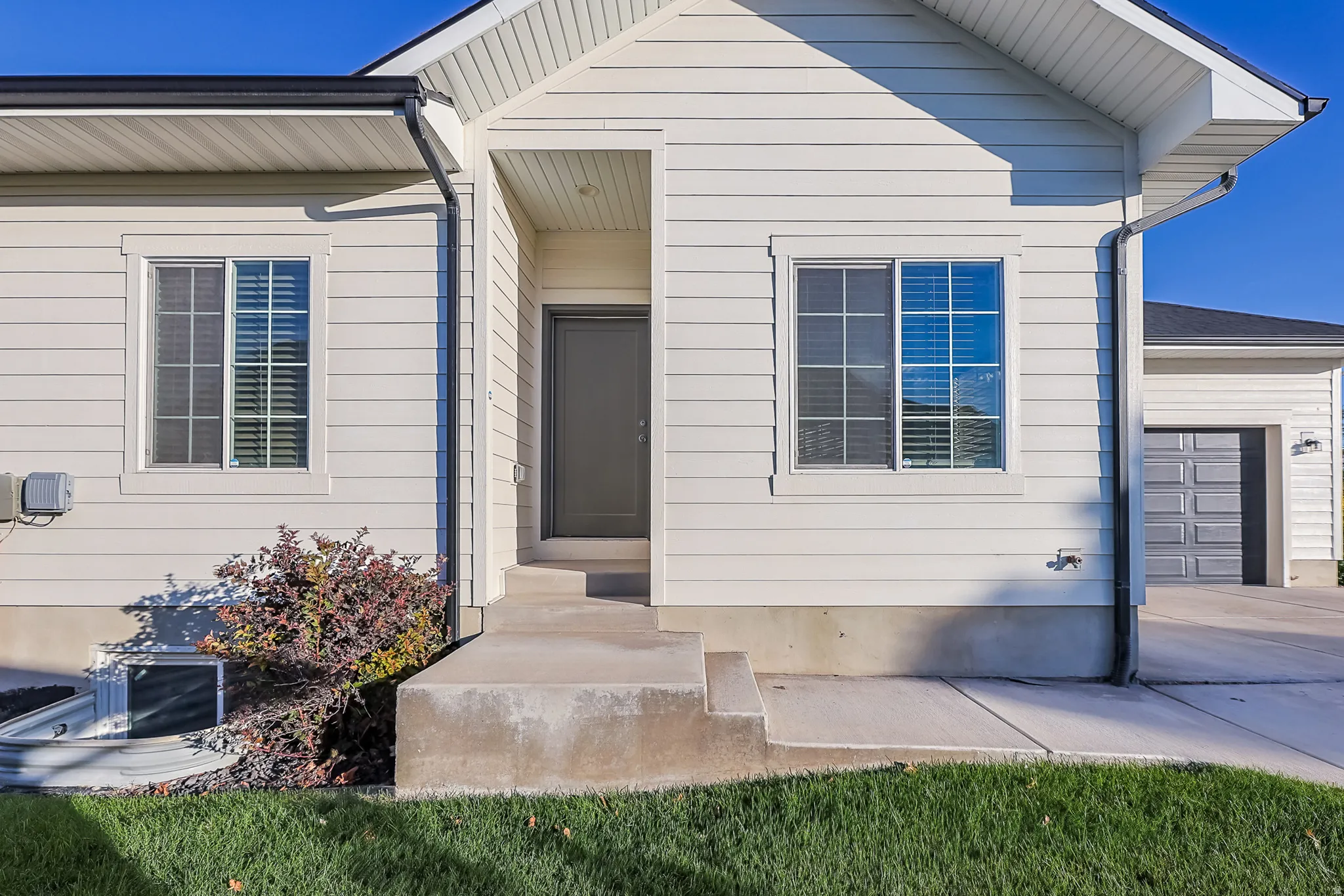 White horizontal siding exterior with a dark entry door, concrete front steps, and a privacy-fenced basement window well