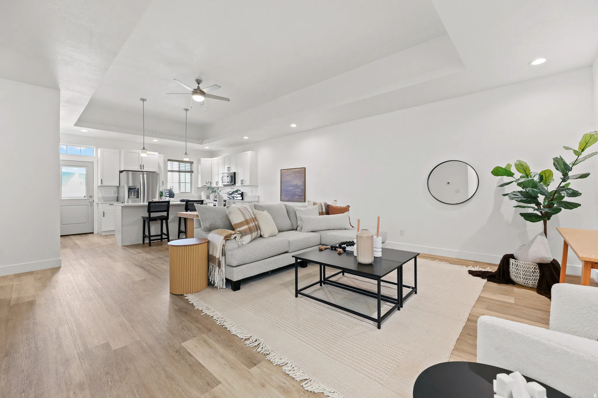 Open-concept living area with tray ceiling, wood-finish flooring, recessed lighting, and a ceiling fan