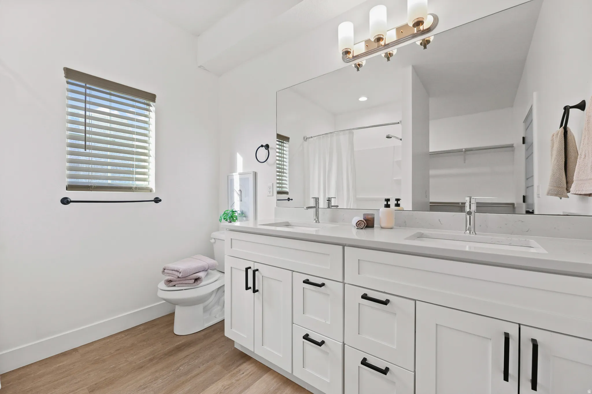 Primary Bedroom Ensuite. Dual vanity with white cabinetry and black hardware, stone countertop, undermount sinks, and wall-mounted light fixture