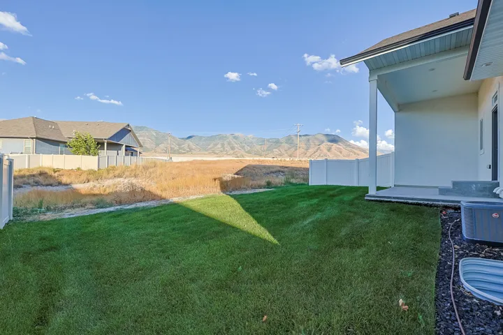 Expansive backyard with a manicured lawn, a white vinyl fence, and a concrete patio