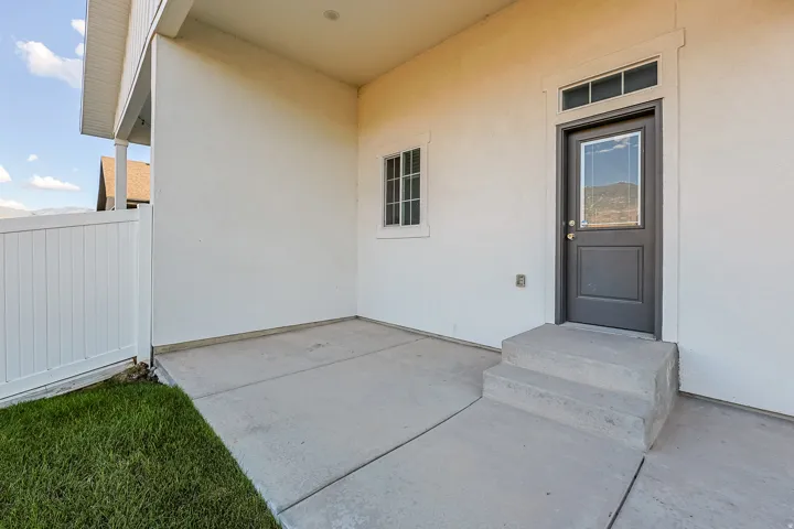 Covered concrete patio with a white privacy fence, and a dark entry door with a transom window
