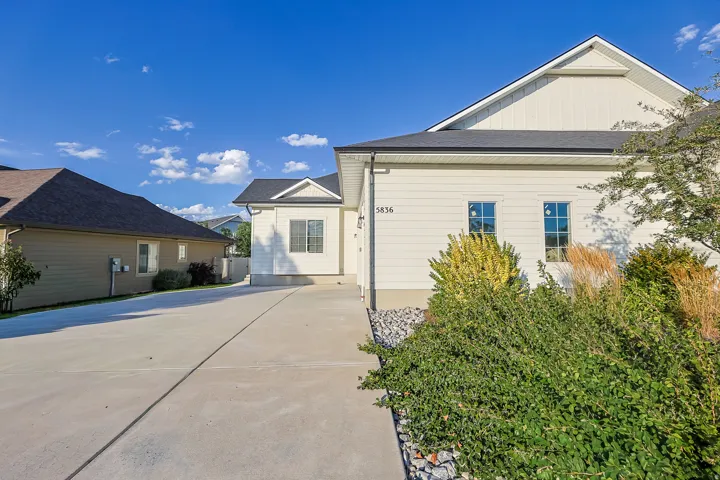 Concrete driveway with stone landscaping and established plantings, featuring a light-colored exterior with a dark shingle roof