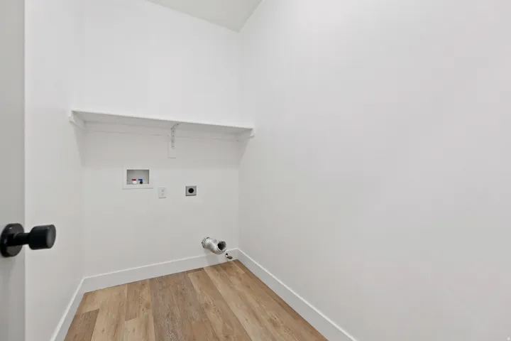 Laundry area featuring wood-finish flooring, white walls, built-in shelving, and utility hookups