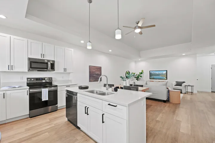 Open-concept living area with wood-finish flooring, white cabinetry, stainless steel appliances, and an island with a double sink