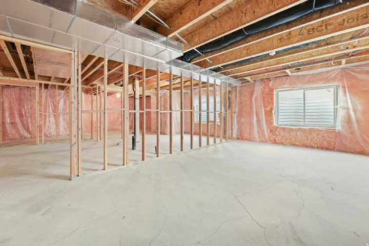 Unfinished basement featuring concrete flooring, exposed wood framing, and two windows