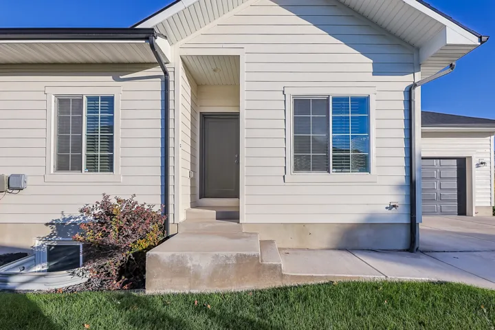 White horizontal siding exterior with a dark entry door, concrete front steps, and a privacy-fenced basement window well