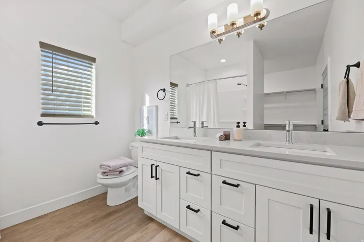 Primary Bedroom Ensuite. Dual vanity with white cabinetry and black hardware, stone countertop, undermount sinks, and wall-mounted light fixture