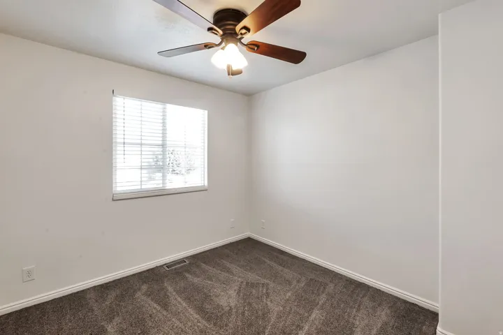 Room featuring neutral wall tones, window with horizontal blinds, ceiling fan with integrated lighting, and patterned carpeting