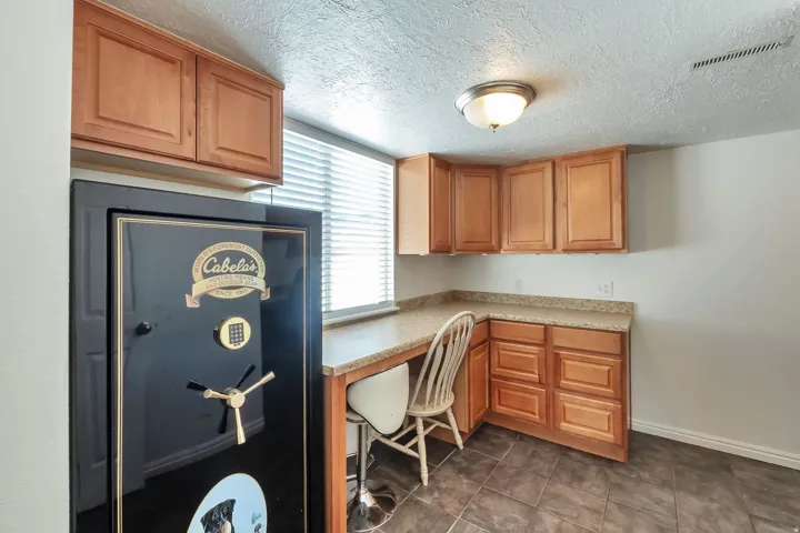 Wood-finish cabinetry, speckled countertop, tile flooring, and integrated desk space with window