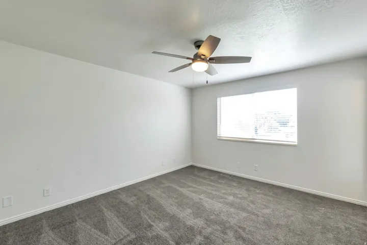 Room with white walls, grey textured carpet, and a ceiling fan with integrated lighting