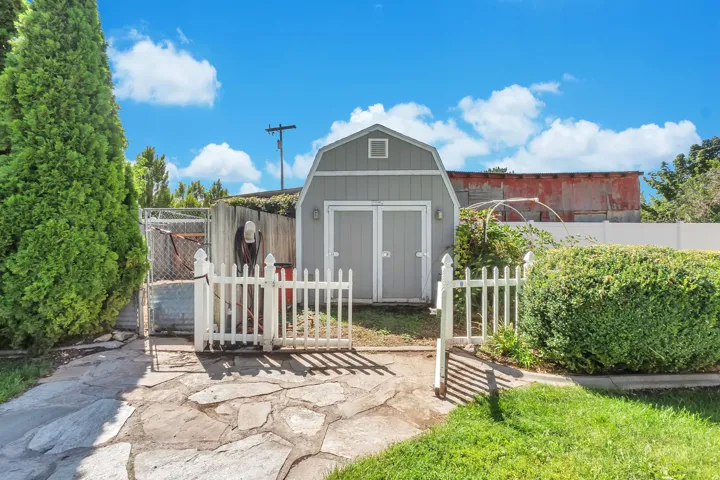 Gabled storage shed with double doors, enclosed by a white picket fence