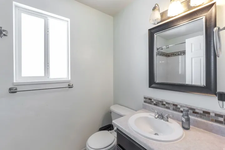 Single vanity with an oval sink, mosaic tile backsplash, framed mirror, and a wall-mounted light fixture