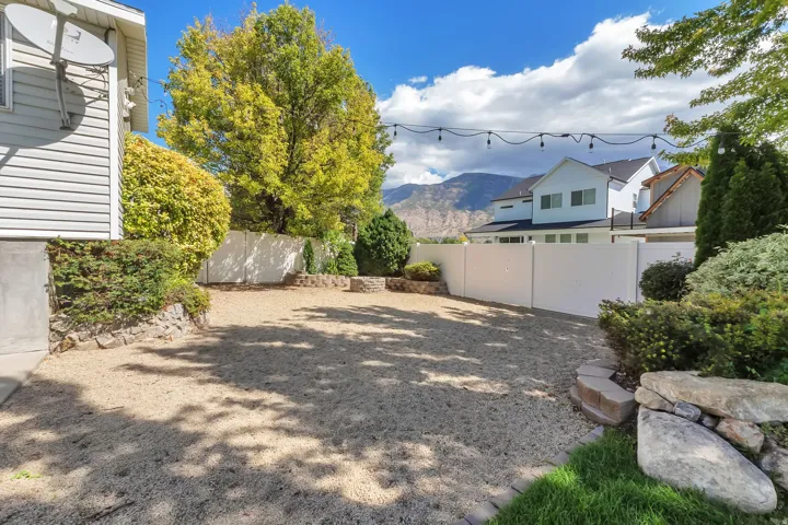 Expansive gravel yard featuring a white privacy fence, string lighting, and mature landscaping