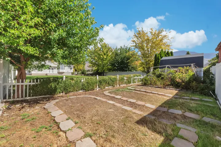Landscaped backyard featuring established planting beds, stone pathways, and mature trees