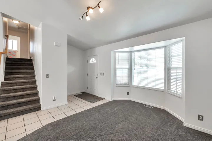 Bay window with blinds, carpeted floor, tiled entry, and staircase with carpeted treads