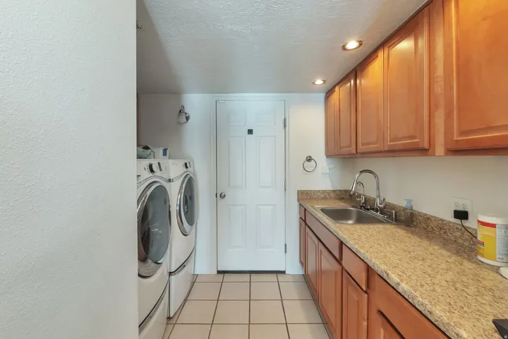 Utility room with a sink, wood cabinetry, stone-finish countertops, and recessed lighting