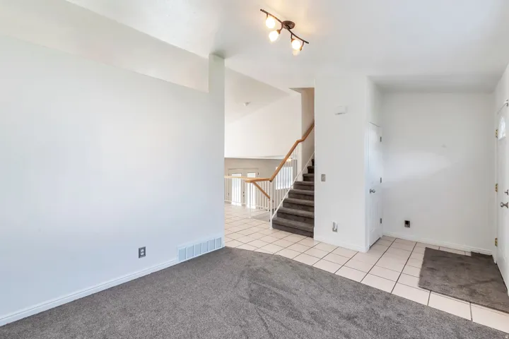 Vaulted ceilings with track lighting, staircase with wood handrail, tiled flooring, and neutral carpeting