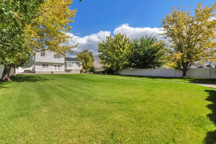 Expansive lawn area with mature trees, a white perimeter fence, and two-story exterior siding