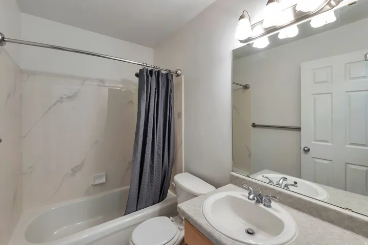 Bathtub with white surround, chrome shower rod, single vanity with integrated sink, chrome faucet, and expansive mirror with overhead lighting