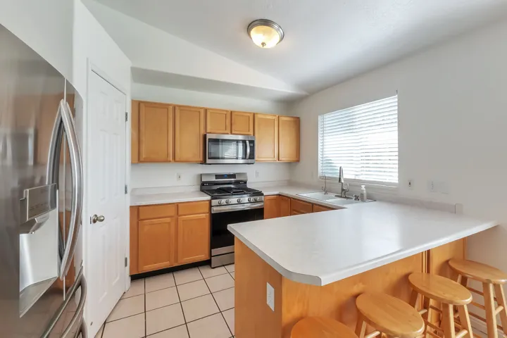 Kitchen featuring light wood cabinetry, stainless steel appliances, white countertops, and tile flooring