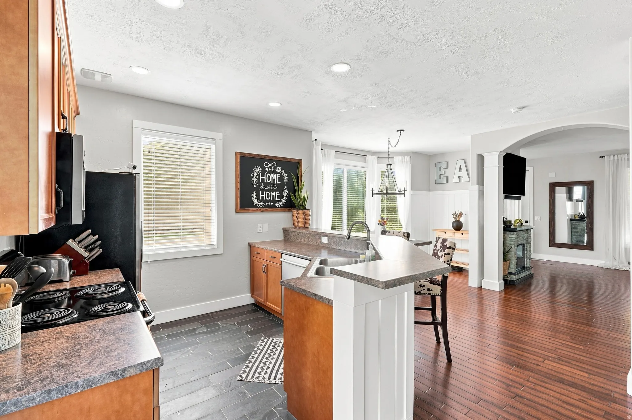 Kitchen featuring wood cabinetry, stone-finish countertops, black appliances, and dark tile flooring