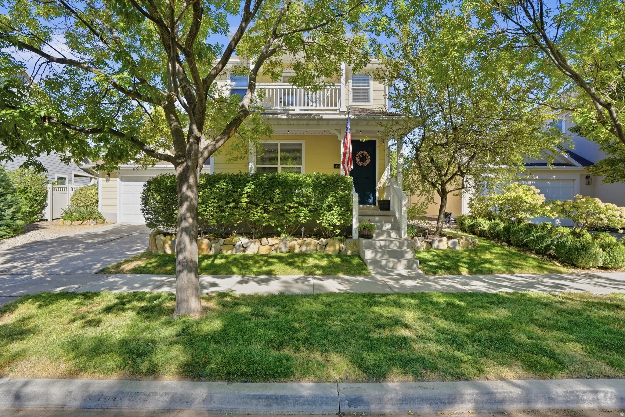 Two-story siding exterior with a front balcony, covered porch, concrete walkway, and paved driveway