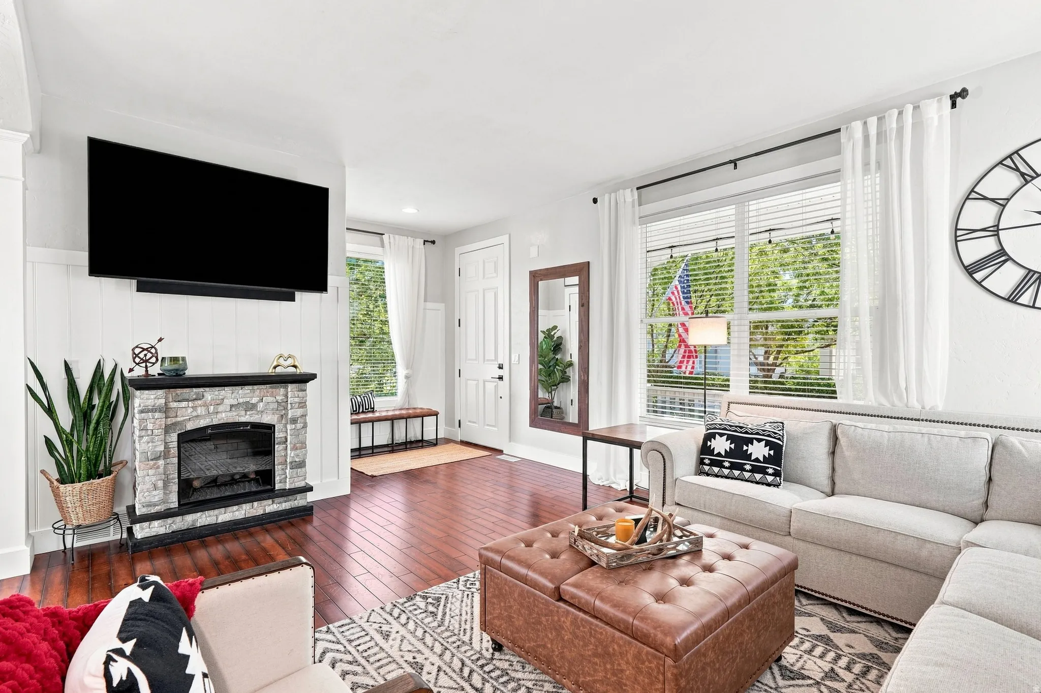 Wood-finish flooring, stone-clad fireplace, white paneled wall, and a white entry door
