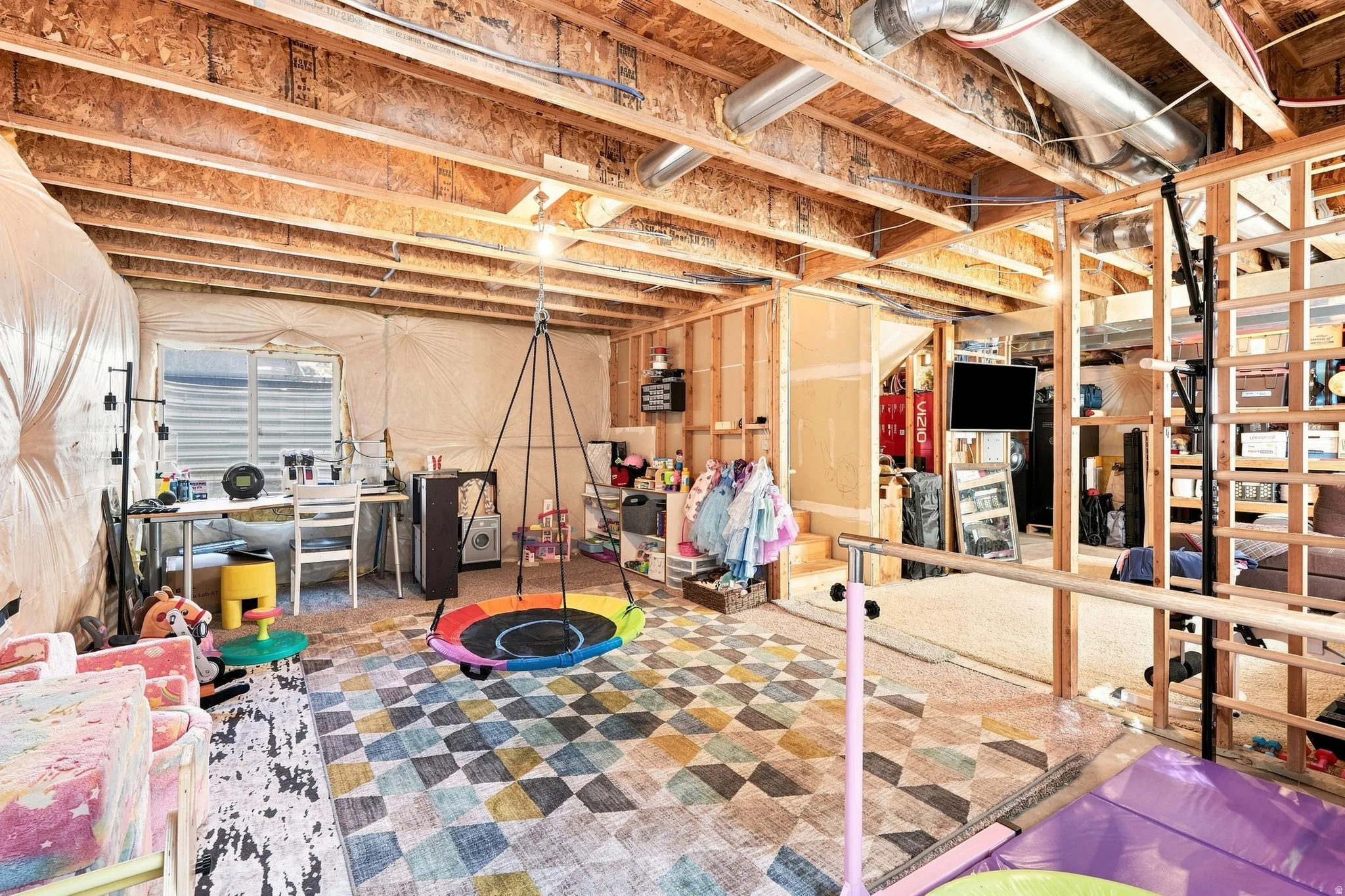 Unfinished basement with exposed ceiling joists and ductwork, framed partitions, and an egress window