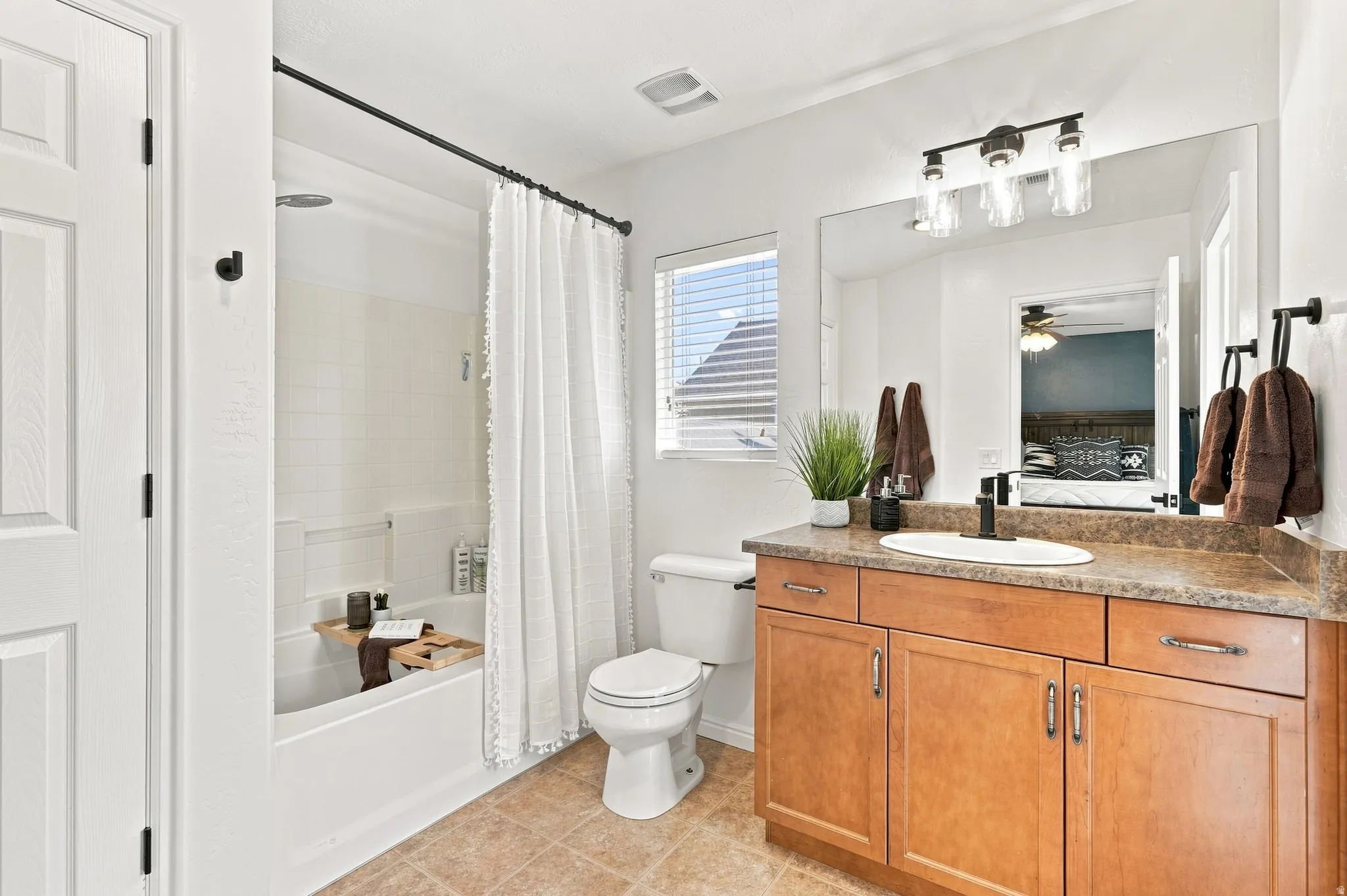 Bathroom featuring a bathtub with a shower, a single vanity with wood-finish cabinetry, a large wall-mounted mirror, and tile flooring
