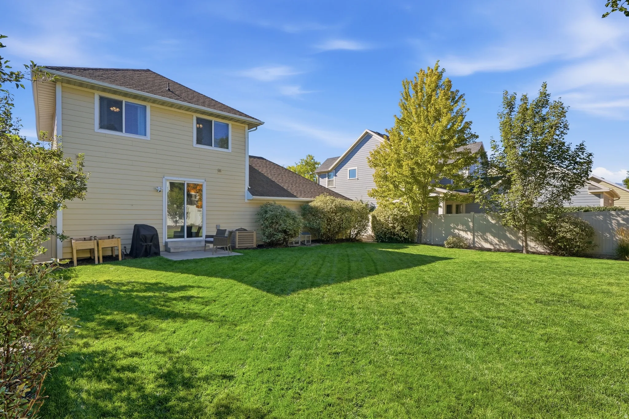 Expansive lawn area with a concrete patio, exterior siding, and mature landscaping
