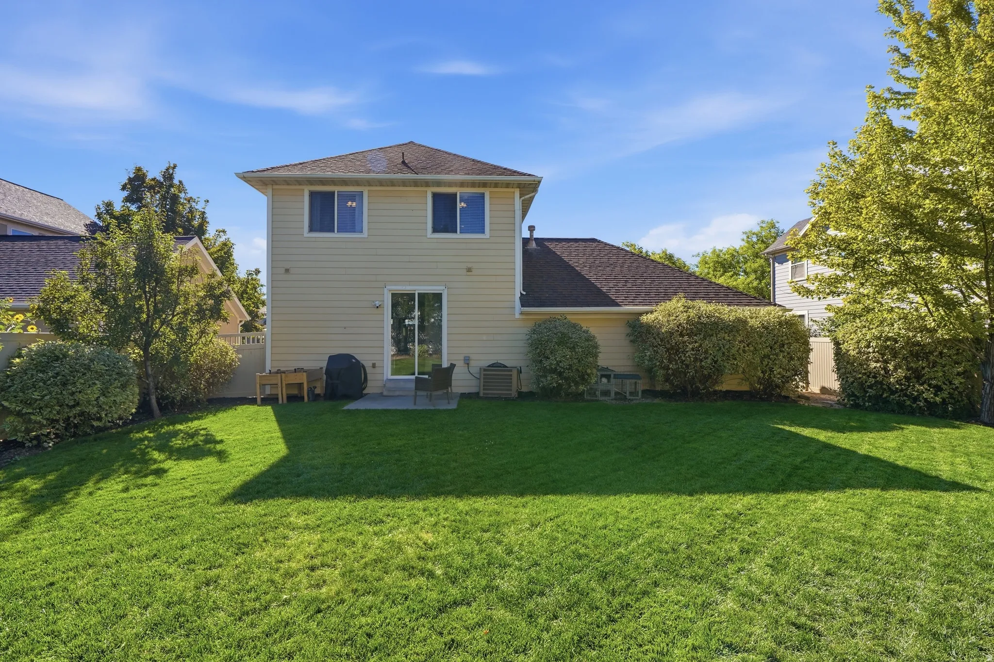 Expansive green lawn with mature landscaping, fenced perimeter, and a patio with direct access to the interior via a sliding glass door