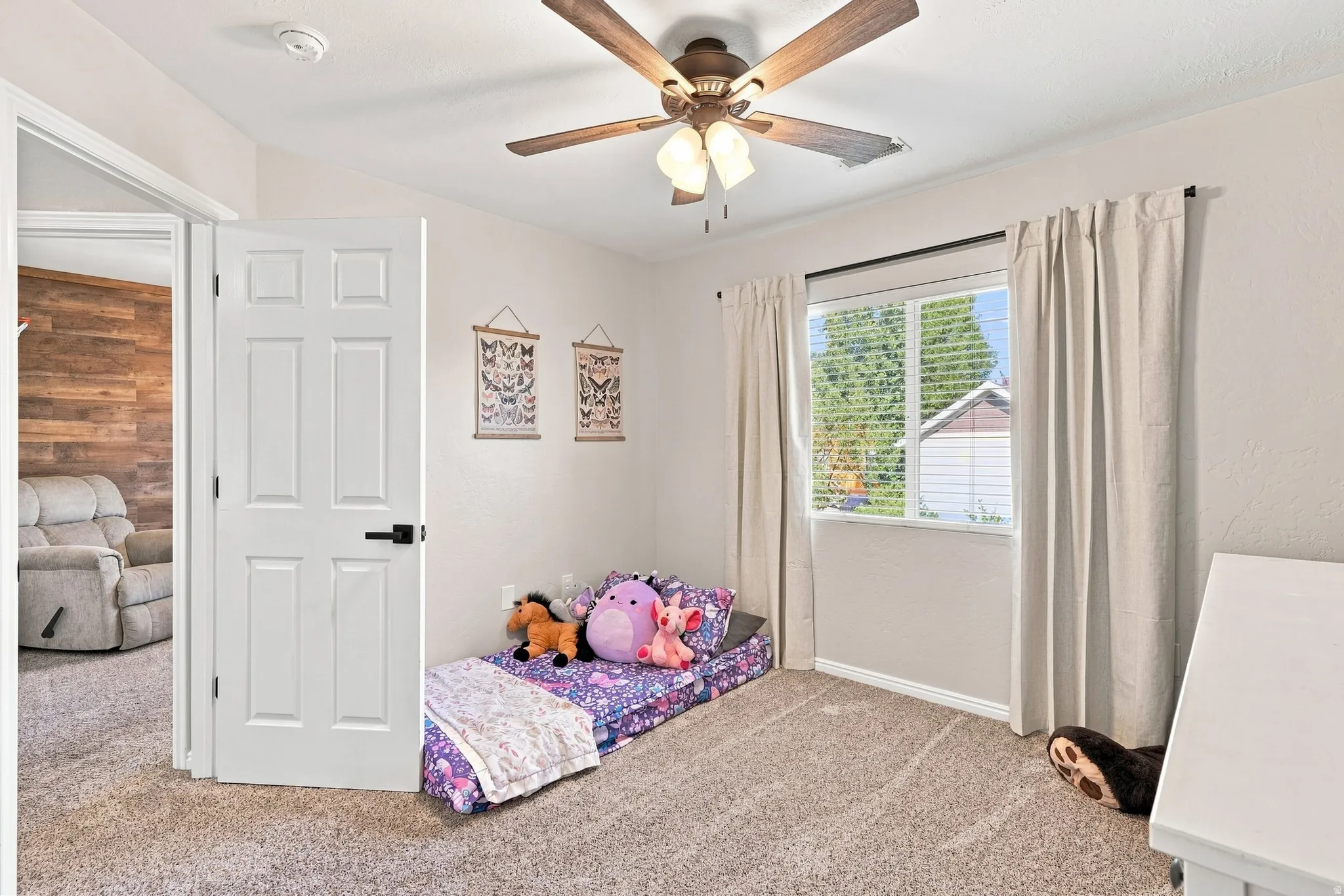 Warm neutral-toned carpeting, ceiling fan with integrated lighting, window with blinds, white trim, and a paneled interior door with black hardware
