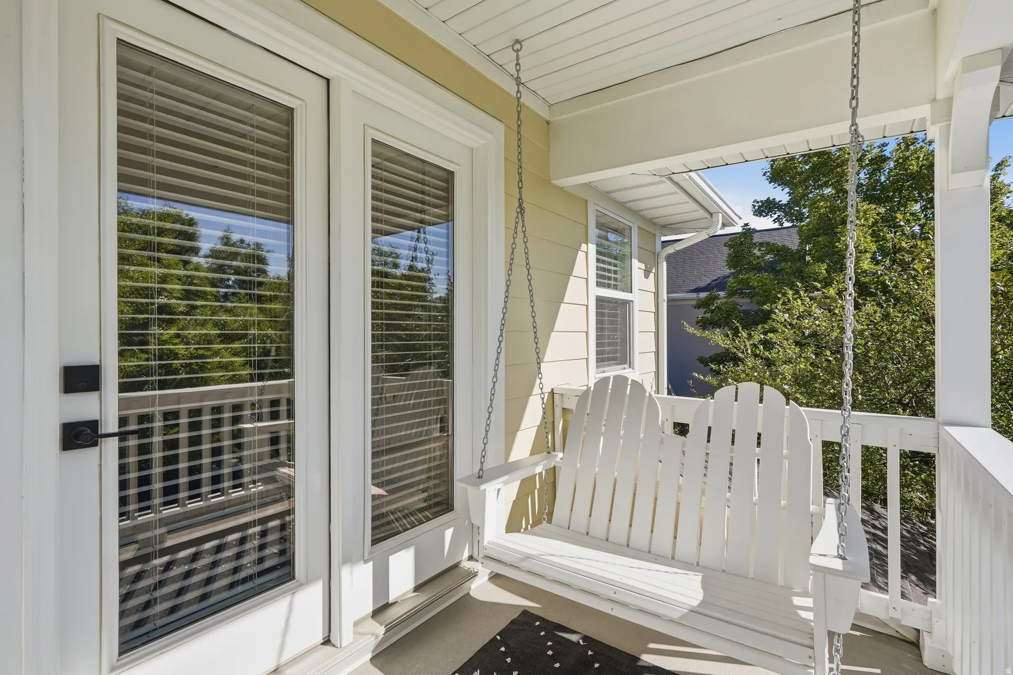 Covered porch with light yellow siding and a white porch swing