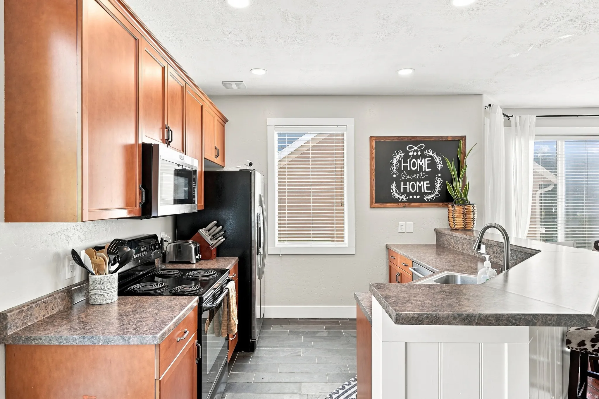 Kitchen featuring wood-finish cabinetry, dark countertops, a built-in microwave, and a stainless steel sink with a gooseneck faucet