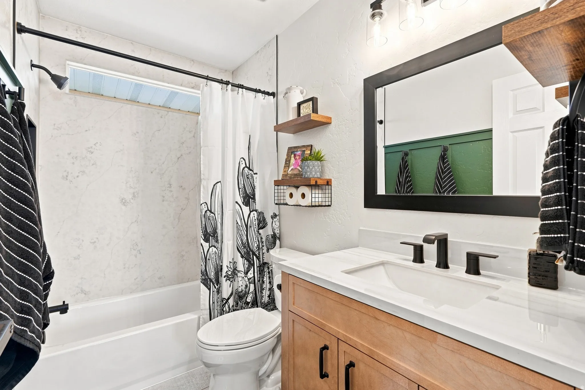 White integrated sink with a black matte faucet, light wood-finish vanity, and a framed mirror