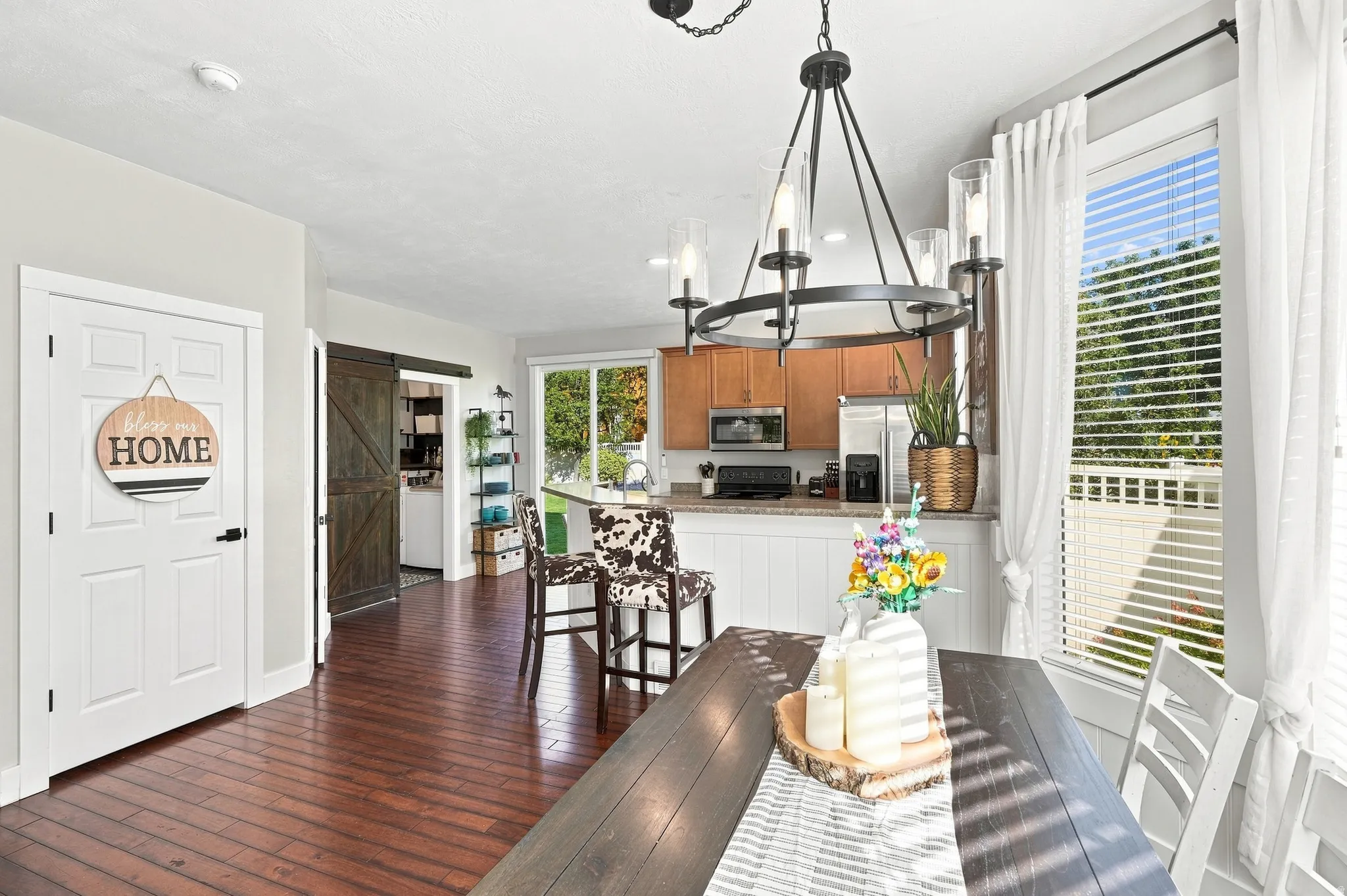 Hardwood-finish flooring, a kitchen island with seating, a dark wood sliding barn door, and a contemporary chandelier