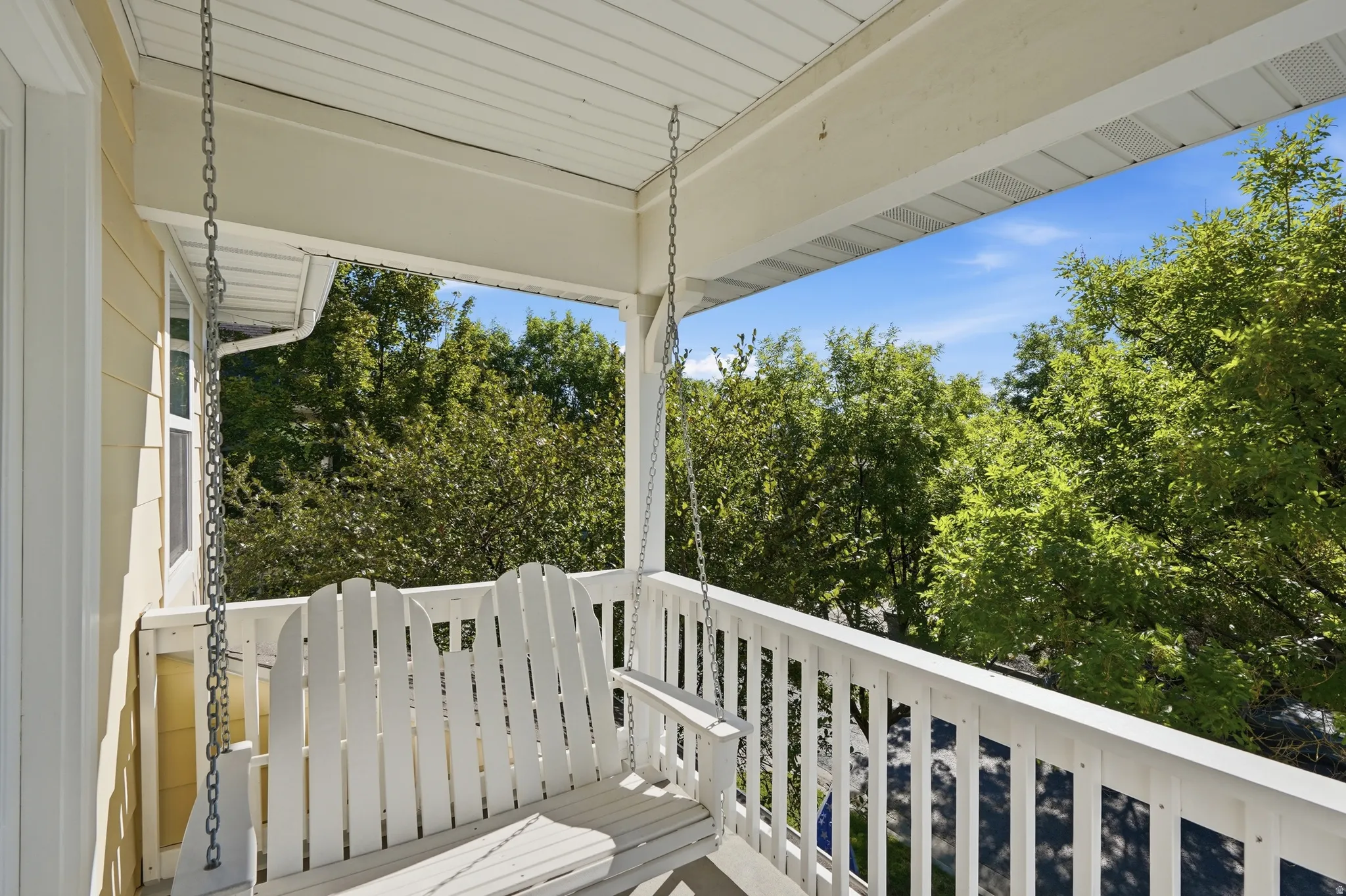 Covered porch with white wood railing, light yellow siding, and a white ceiling