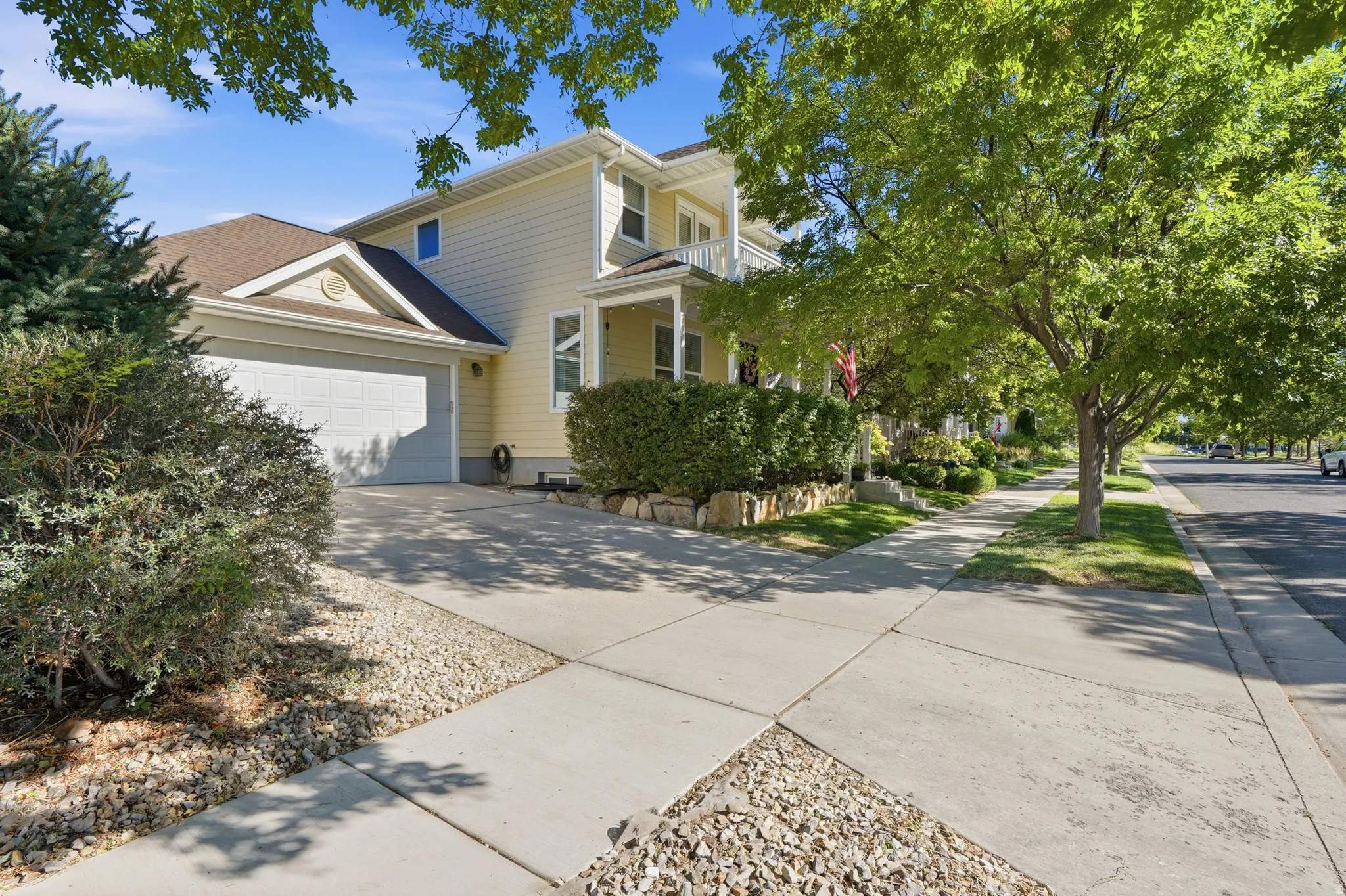 Two-story residence with light yellow siding, attached two-car garage, and a covered front porch