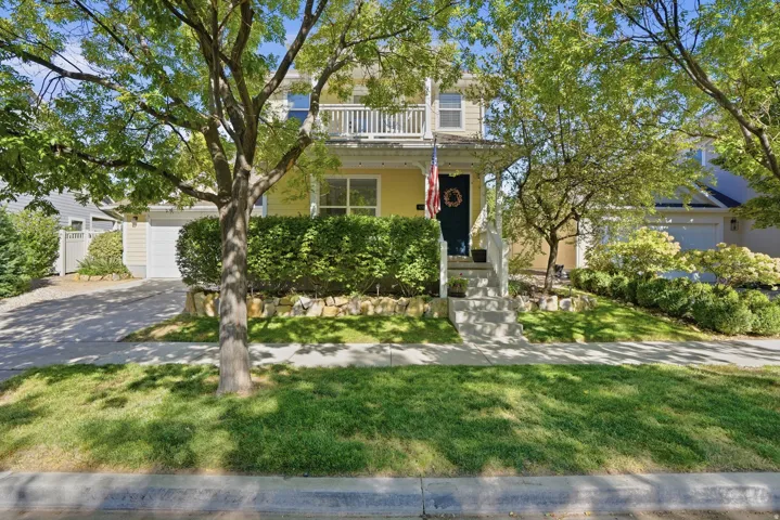 Two-story siding exterior with a front balcony, covered porch, concrete walkway, and paved driveway