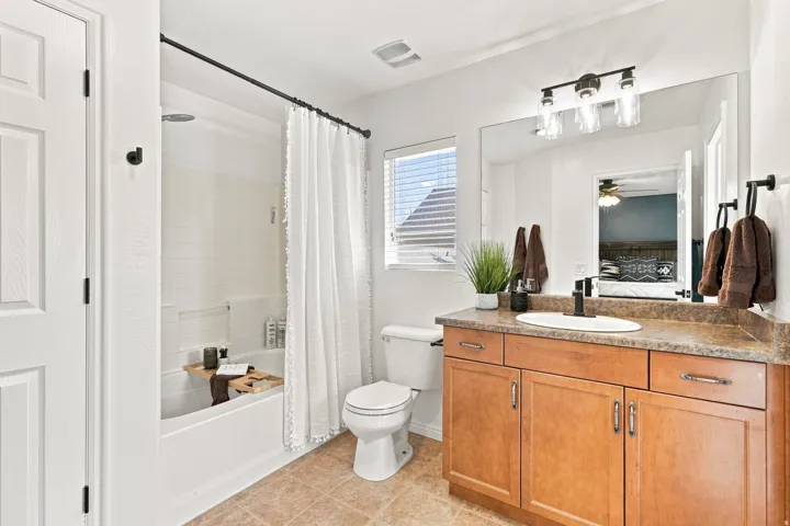 Bathroom featuring a bathtub with a shower, a single vanity with wood-finish cabinetry, a large wall-mounted mirror, and tile flooring